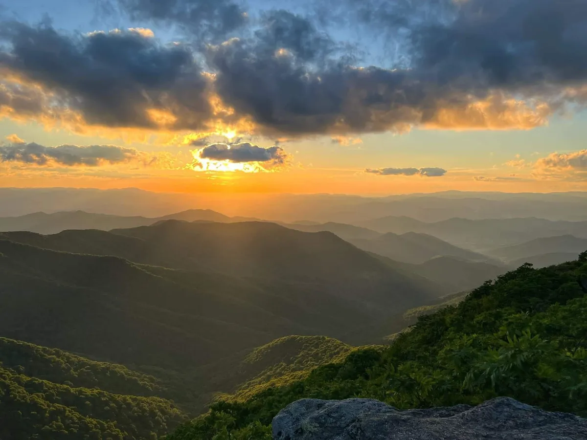 A breathtaking view of distant mountains under a setting sun, with dramatic clouds and tranquil surroundings. The scenery invites moments of reflection and highlights the beauty of the area’s natural setting.