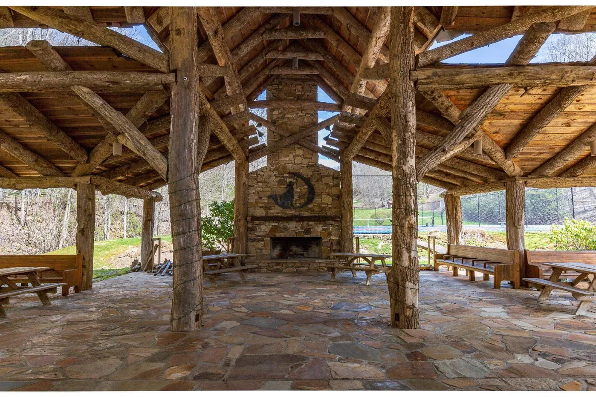 An inviting exterior living area with a large stone fireplace, wooden beams, and open space, perfect for gatherings or relaxing in the fresh air. The area hints at communal meals, socializing, and high-elevation serenity.