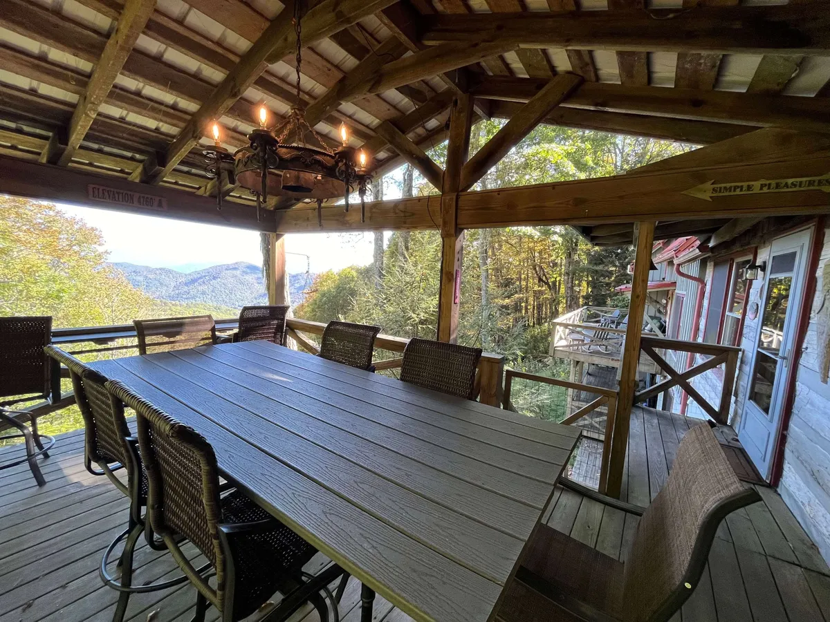 A spacious wooden deck featuring a large dining table beneath a chandelier, with panoramic mountain views stretching into the distance. The deck's position showcases multi-level outdoor living and effortless transitions to nature.