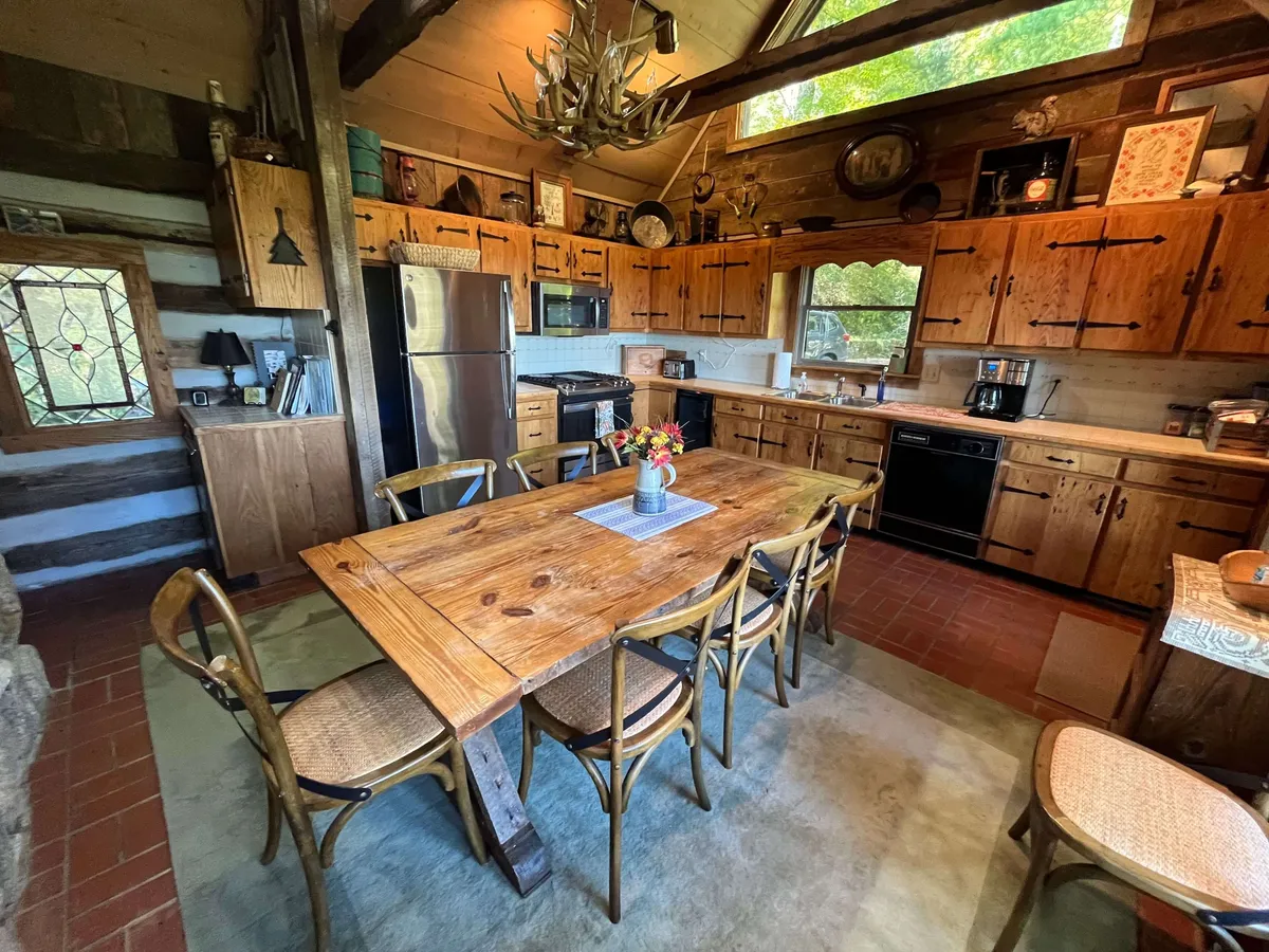 The dining area is presented with a large wooden table, vintage cabinetry, and generous windows that allow sunlight to flood the space. The rustic decor and natural materials reflect the home’s history and charm, offering a welcoming spot for meals and conversations.