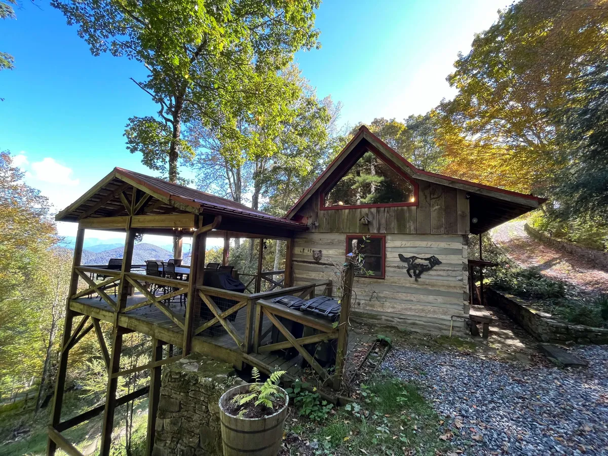 This exterior image highlights the wooden deck attached to the cabin, surrounded by trees and offering sweeping mountain views. The deck is ideal for outdoor relaxation and barbecues, seamlessly connecting indoor hospitality with the beauty of the outdoors.
