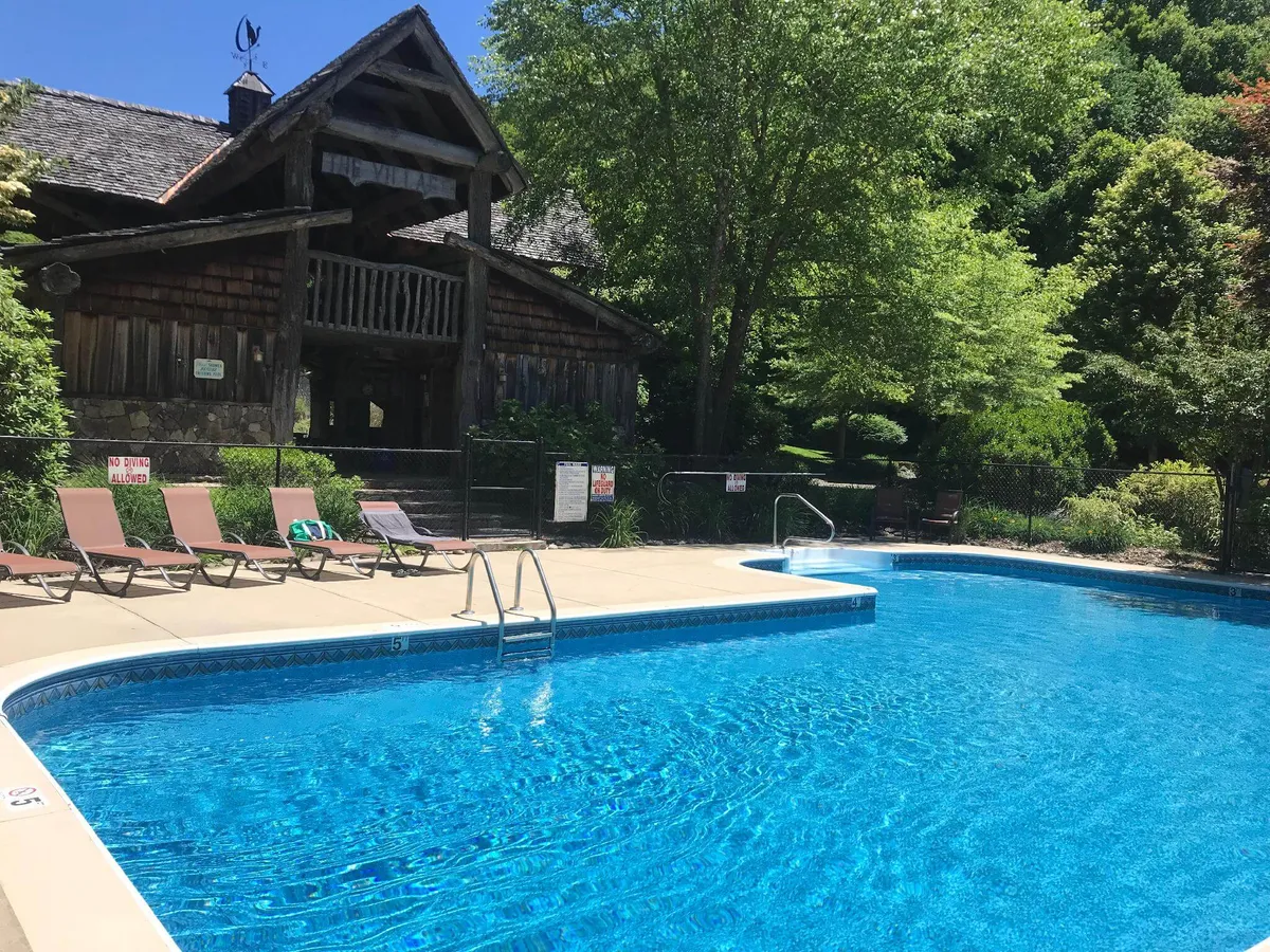 A vibrant outdoor swimming pool surrounded by lounge chairs, with a charming wooden cabin nearby. The pool area is bathed in warm light, suggesting the potential for sunset swims and relaxed poolside gatherings.