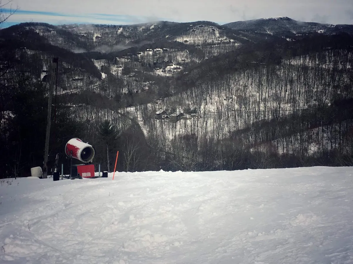 A panoramic view of snow-covered slopes equipped with a snow cannon, with a vast mountain range stretching into the distance. The slopes are fresh and inviting, suggesting opportunities for skiing, snowboarding, and winter hiking. The scene exudes an adventurous winter spirit, perfect for outdoor enthusiasts.