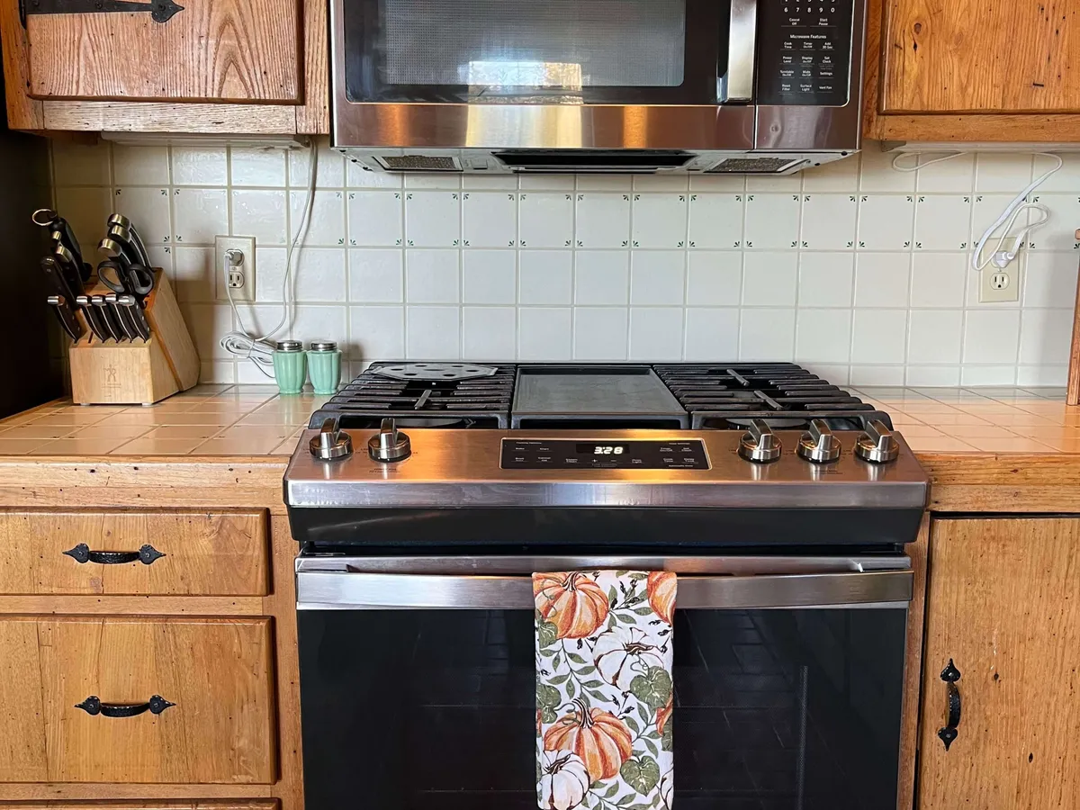 A closer view of the kitchen workspace, featuring a stove, knife block, and dish towel. The mood is cozy and inviting, emphasizing cooking activities and the hands-on experience of preparing meals for family and friends.